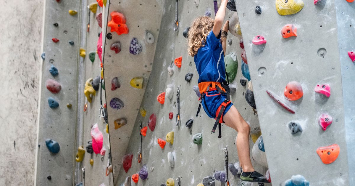 Woman Indoor Rock Climbing On A Colorful Artificial Climbing Wall.